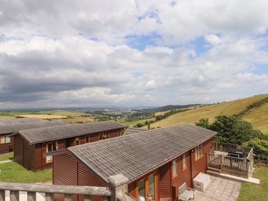 A view of wooden cabins on a hillside with a patio and outdoor furniture surrounded by fields and hills at Tamar View Lodge in Millbrook