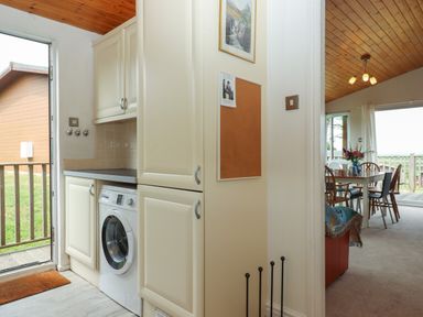 A kitchen area with a washing machine and cabinets next to a dining room with a table and chairs at Tamar View Lodge in Millbrook