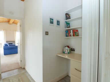 A small desk area with shelves of books and a decorative house next to a hallway leading to a room with a blue sofa at Tamar View Lodge Millbrook