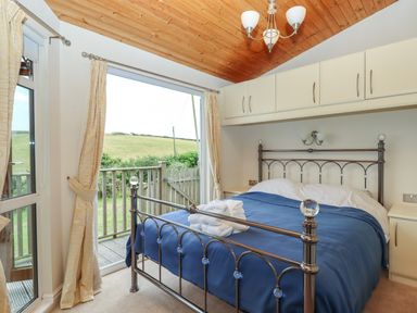 A bedroom with a metal bed frame and blue bedspread next to a sliding door opening to a deck at Tamar View Lodge in Millbrook