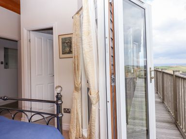 A bedroom with a metal bed frame near an open door leading to a wooden balcony at Tamar View Lodge in Millbrook