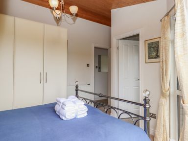 A bedroom with a blue bedspread white folded towels on the bed cream wardrobes a wooden ceiling and cream curtains at Tamar View Lodge in Millbrook