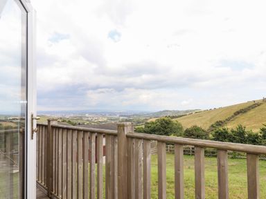 A wooden deck railing overlooking green fields trees and hills under a cloudy sky at Tamar View Lodge in Millbrook