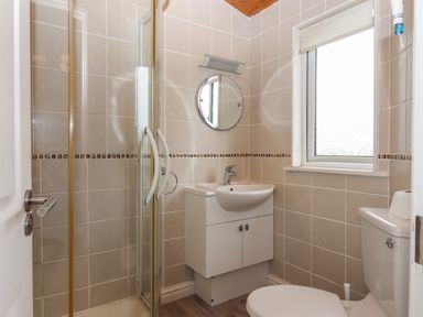 A bathroom with a shower enclosure sink with cabinet round mirror window and toilet at Tamar View Lodge Millbrook