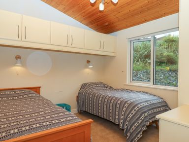 A bedroom with two single beds under wall cabinets and a window showing greenery at Tamar View Lodge in Millbrook