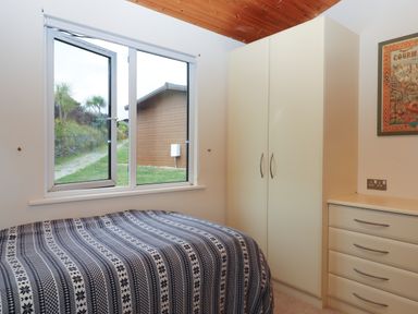 A bedroom with a bed covered with a patterned blanket a wardrobe and a chest of drawers near a window at Tamar View Lodge in Millbrook