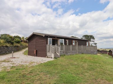 A wooden lodge with a porch and railing on a grassy area under a cloudy sky at Tamar View Lodge in Millbrook