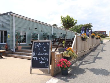 An outdoor seating area with wooden benches and a signboard indicating bar and restaurant direction at Tamar View Lodge in Millbrook