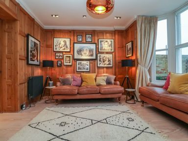 A sitting room with brown leather sofas colourful cushions black lamps and framed photos on wooden paneled walls at 42 Crag Path in Aldeburgh