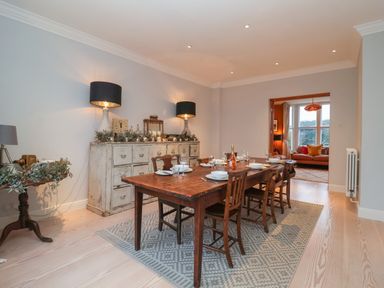 A dining room with a wooden table and chairs a sideboard with lamps and decorations and a living room visible through a doorway at 42 Crag Path in Aldeburgh
