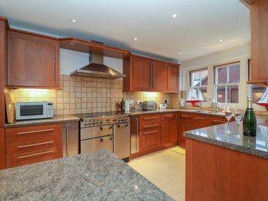 A kitchen with wooden cabinets granite countertops a microwave stove and two windows at 42 Crag Path Aldeburgh