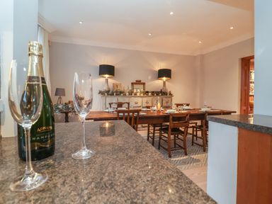 A dining room with a wooden table set with plates and glasses and a champagne bottle on the counter at 42 Crag Path in Aldeburgh