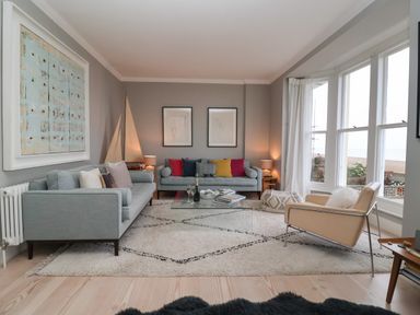 A living room with two blue sofas a beige armchair glass coffee table and large windows at 42 Crag Path in Aldeburgh