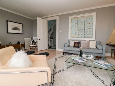 A living room with a beige chair and a blue sofa a glass coffee table with books and a bottle at 42 Crag Path in Aldeburgh