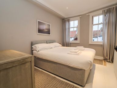 A bedroom with a double bed white bedding two windows and a wooden chest at 42 Crag Path in Aldeburgh