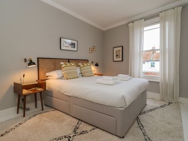 A bedroom with a bed with patterned pillows bedside tables lamps wall art and a window with curtains at 42 Crag Path in Aldeburgh