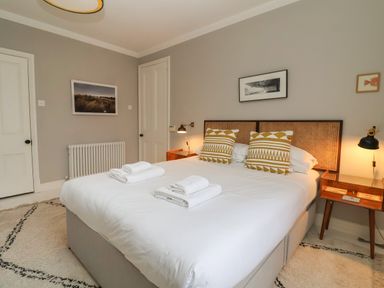 A bedroom with a double bed white bedding patterned pillows bedside tables lamps and framed pictures on walls at 42 Crag Path Aldeburgh