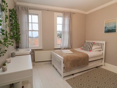 A bedroom with a white bed a brown blanket two windows and a white sink at 42 Crag Path in Aldeburgh