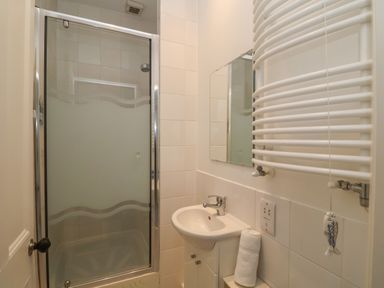 A small bathroom with a shower, sink, mirror, and towel radiator at 42 Crag Path in Aldeburgh
