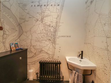 A small bathroom with a corner sink black radiator and map wallpaper at 42 Crag Path Aldeburgh