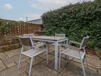 An outdoor patio area with a table and four chairs surrounded by a brick wall and greenery at 42 Crag Path in Aldeburgh