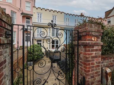 A black wrought iron gate and brick pillar with house number 42 leading to colorful townhouses at 42 Crag Path in Aldeburgh