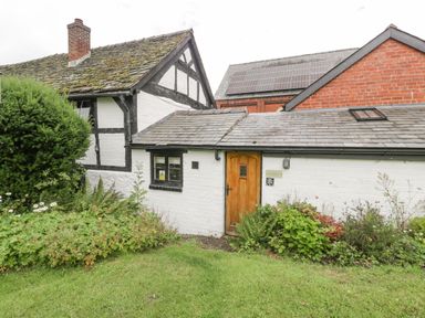 A white brick house with a wooden door surrounded by plants and grass at The Old Bakehouse in Pembridge