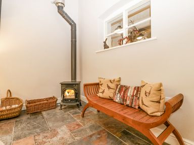 A room with a wood burning stove a wooden bench with cushions and wicker baskets at The Old Bakehouse in Pembridge