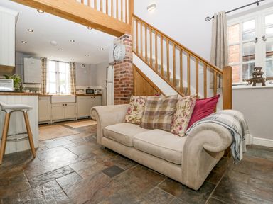 A kitchen and sitting area with a beige sofa and pillows under wooden stairs at The Old Bakehouse in Pembridge