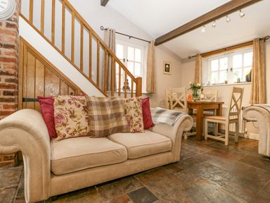 A living room with a beige sofa and dining table with chairs near windows at The Old Bakehouse in Pembridge