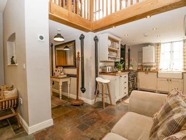 A kitchen and living area with a stove, white cabinets, countertop, bar stool, and a beige sofa at The Old Bakehouse in Pembridge