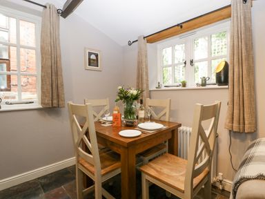 A dining area with a wooden table and four chairs near two windows at The Old Bakehouse in Pembridge