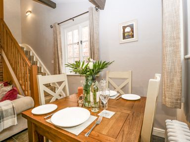 A dining area with a wooden table set for four and a staircase in the background at The Old Bakehouse in Pembridge