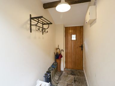A narrow entryway with a wooden door boots lined against the wall and a metal coat rack at The Old Bakehouse in Pembridge