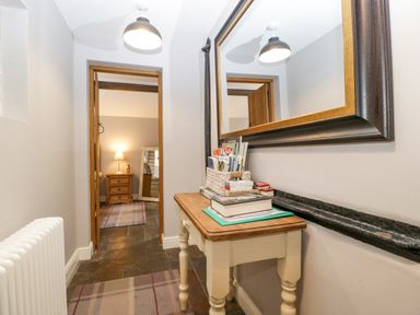 Hallway with a wooden table holding books and magazines and a large wall mirror above at The Old Bakehouse in Pembridge