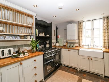 A kitchen with wooden countertops white cabinets a black stove a white sink and dishes on shelves at The Old Bakehouse in Pembridge