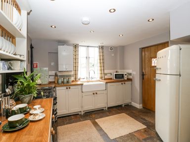 A kitchen with cream cabinets wooden countertops a white fridge and a window with checked curtains at The Old Bakehouse in Pembridge