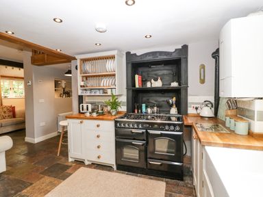 A kitchen with a black stove, wooden countertops, white cabinets, and dishes on a rack at The Old Bakehouse in Pembridge