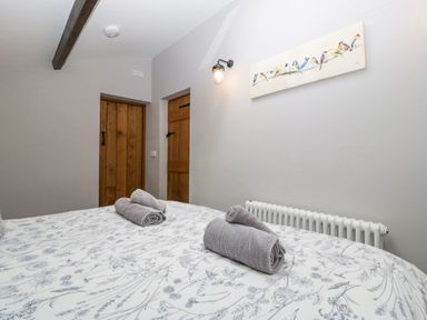 A bedroom with a floral bedspread two rolled towels on the bed wooden doors a radiator and bird artwork on the wall at The Old Bakehouse in Pembridge