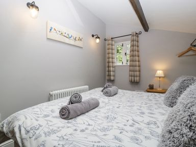 A bedroom with a bed covered by a floral duvet and three rolled towels on top at The Old Bakehouse in Pembridge