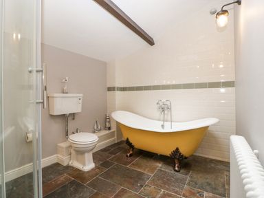 A bathroom with a yellow clawfoot bathtub a toilet and tiled floor at The Old Bakehouse in Pembridge