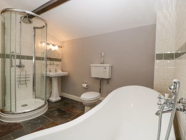 A bathroom with a curved glass shower, pedestal sink, toilet, and a freestanding bathtub at The Old Bakehouse in Pembridge