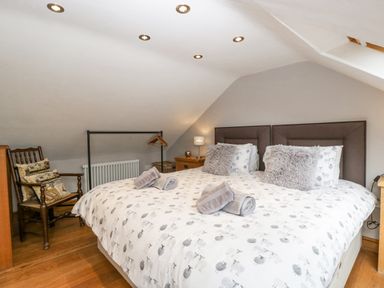 A bedroom with a double bed pillows bedside tables a wooden chair and a clothes rack at The Old Bakehouse in Pembridge