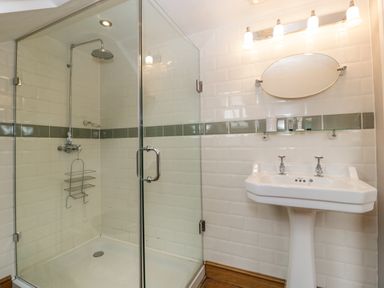 A bathroom with a glass enclosed shower and a pedestal sink with an oval mirror at The Old Bakehouse in Pembridge