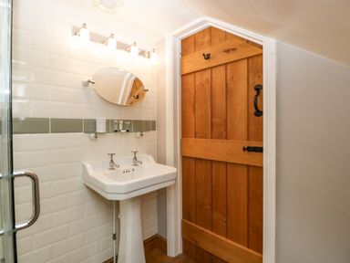 A bathroom with a white pedestal sink mirror and wooden door at The Old Bakehouse in Pembridge