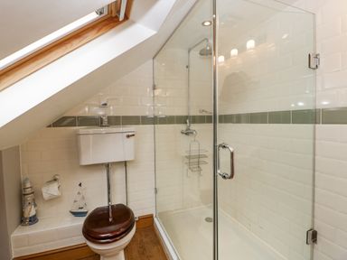 A bathroom with a toilet and a glass shower enclosure under a slanted ceiling at The Old Bakehouse in Pembridge