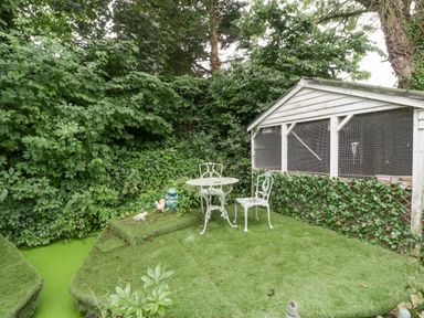 An outdoor garden area with a white metal table and two chairs next to a small shed surrounded by greenery at The Old Bakehouse in Pembridge