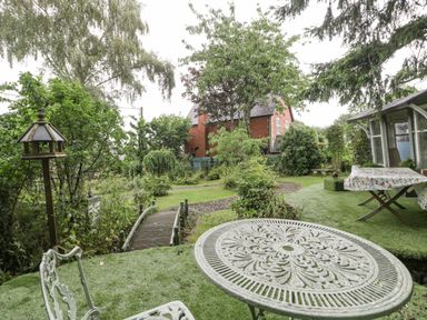 A garden with a metal table and chairs a small wooden bridge and a brick house in the background at The Old Bakehouse in Pembridge