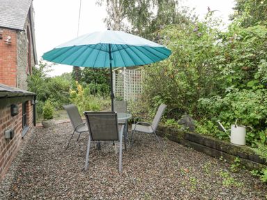 A garden seating area with a table chairs and a blue umbrella beside a brick and stone building at The Old Bakehouse in Pembridge