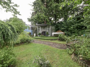 A garden with a grass lawn a gravel path a wooden shed a small gazebo with chairs and a bench with a table at The Old Bakehouse in Pembridge